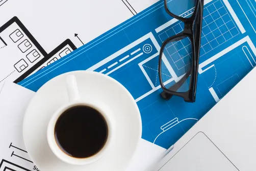 close-up-coffee-cup-with-blueprints-desk